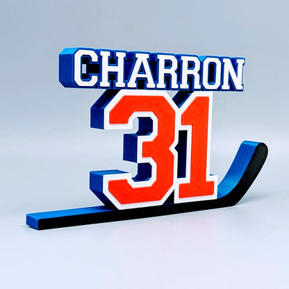 Personalized hockey jersey number nameplate "CHARRON 31" in orange, blue and white on a hockey stick
