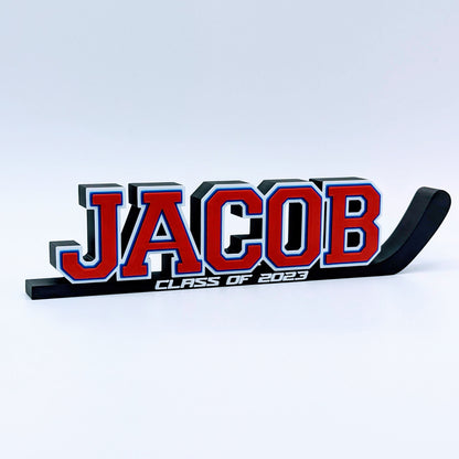Hockey stick nameplate "JACOB" in red, white and blue with "Class of 2023"
