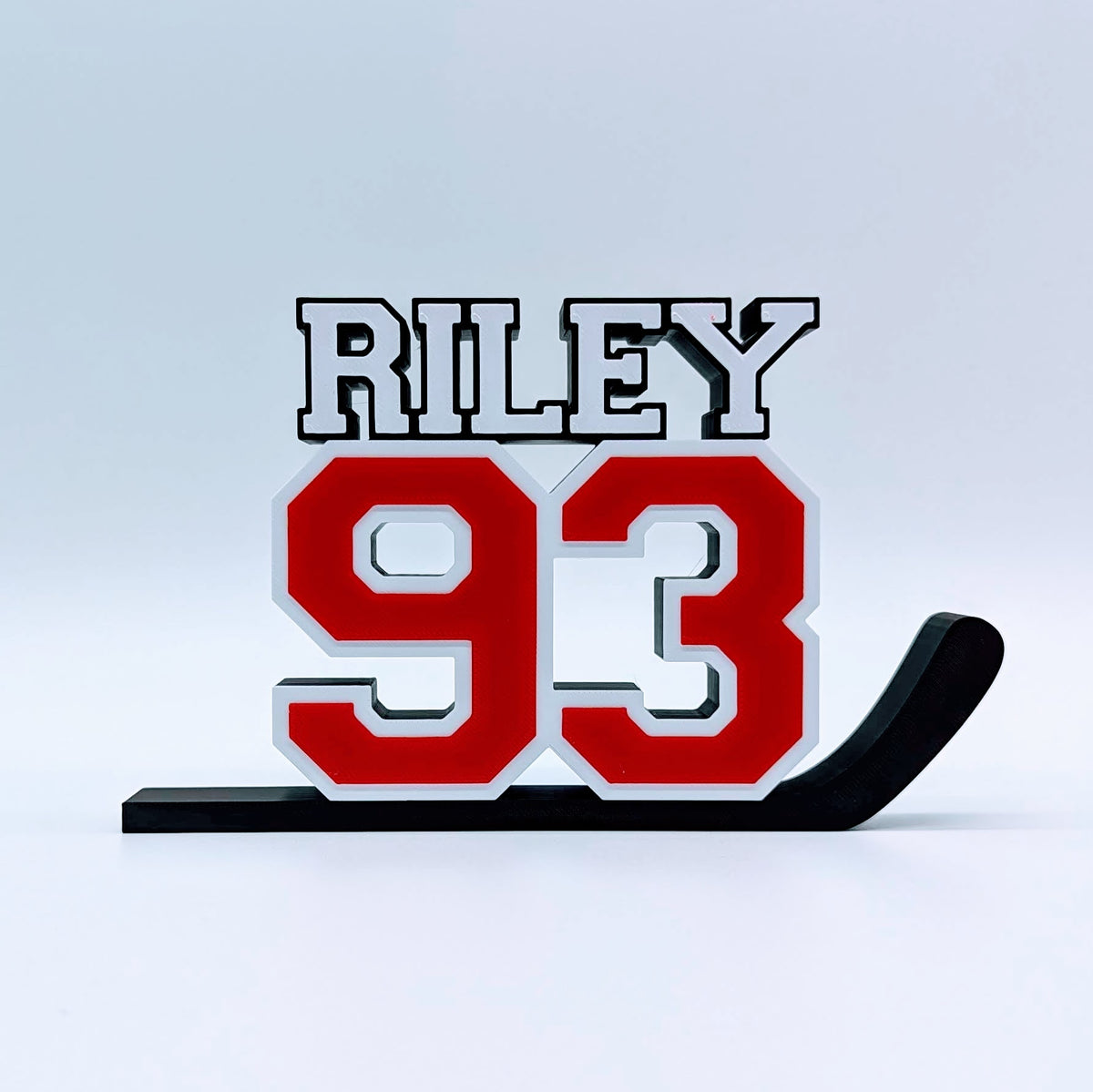 Personalized hockey jersey number nameplate "RILEY 93" in red, white and black on a hockey stick
