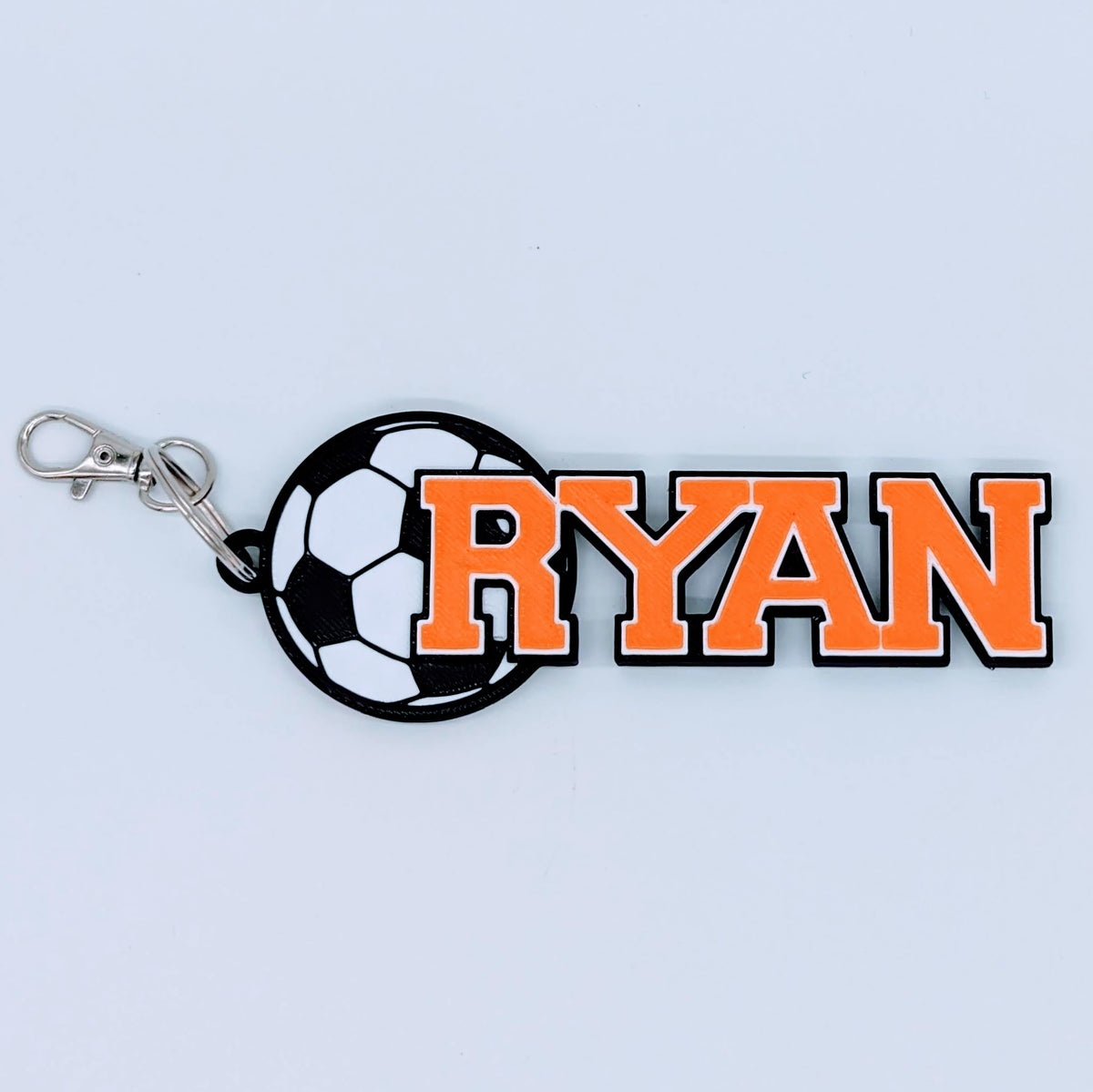 Soccer bag tag "RYAN" in orange with black and white soccer ball