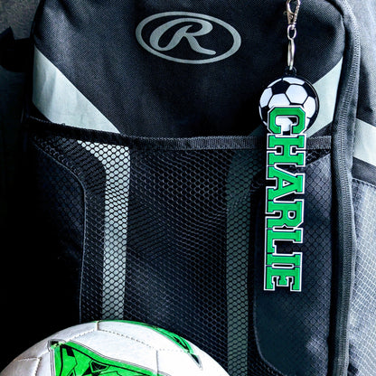 Green soccer bag tag "CHARLIE" on a backpack next to a soccer ball